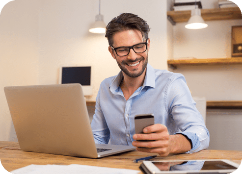 Homme souriant devant un ordinateur et téléphone