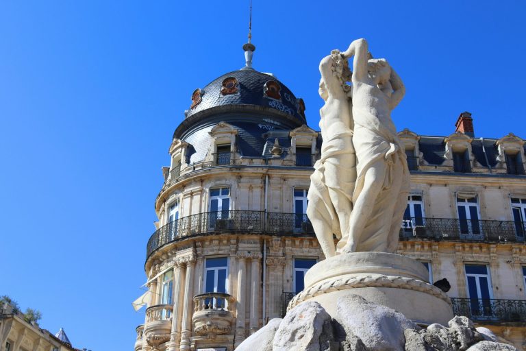 Fontaine des Trois Grâces sur la place de la Comédie à Montpellier, devant un immeuble Belle Époque, sous un ciel bleu