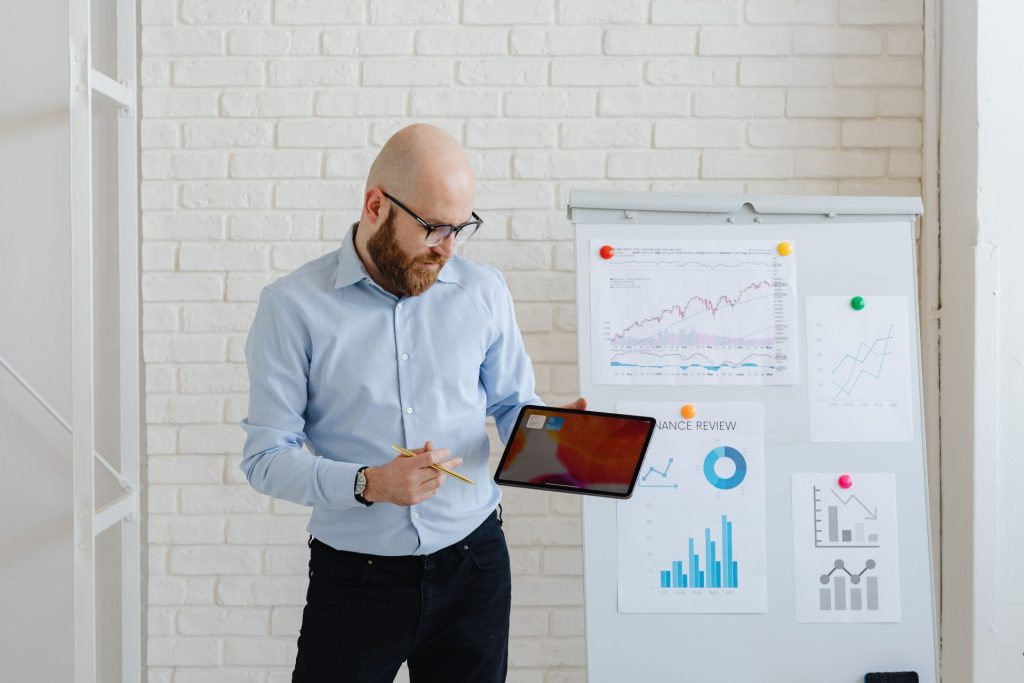Un manager présente des graphiques sur sa tablette devant un paperboard, lors de la restitution des résultats d'une enquête
