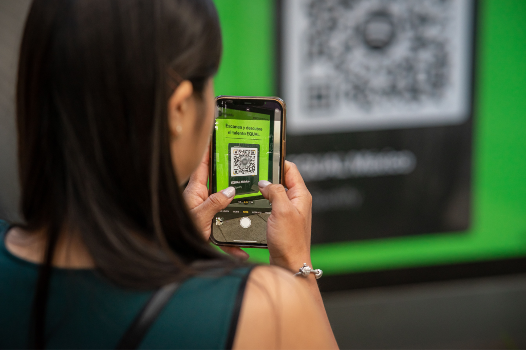 Une femme scanne avec son smartphone un QR code affiché sur un panneau pour accéder à un contenu en ligne