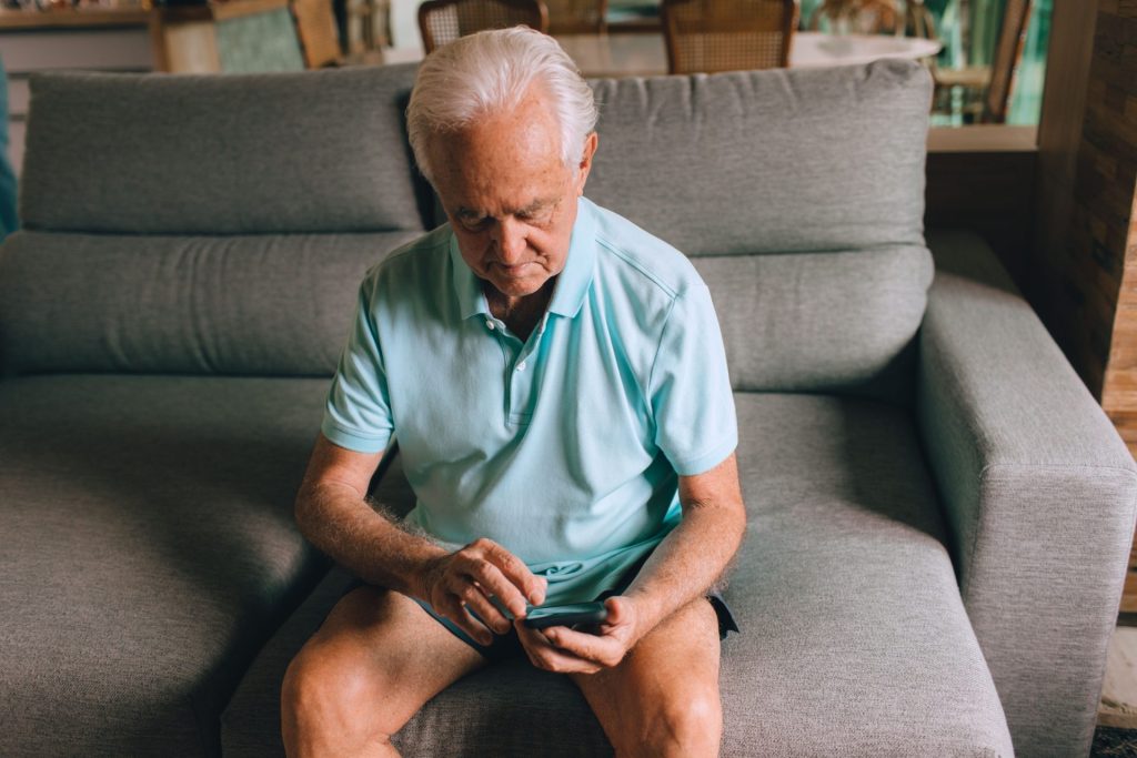Patient senior consultant son smartphone à domicile, illustration de l'adoption du numérique par les patients de la Fondation Santé Service.